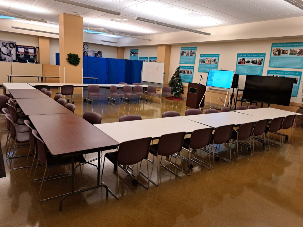 The Poverello room set up with tables and chairs in an L shape