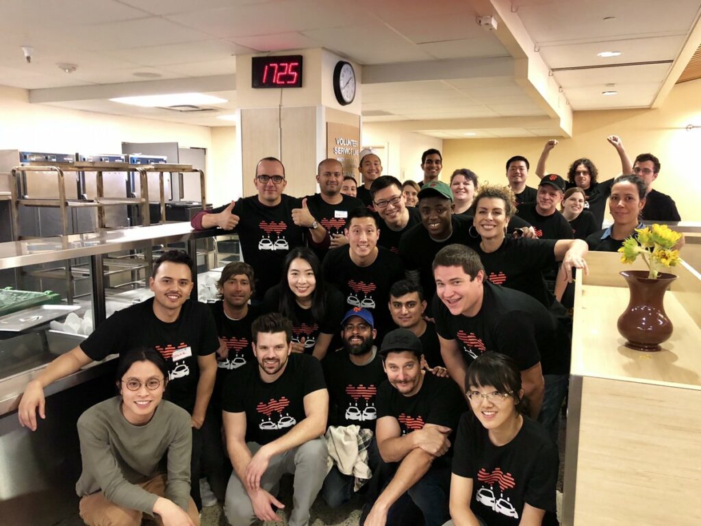 A group of corporate volunteers in matching black shirts pose in the St. Anthony's dining room