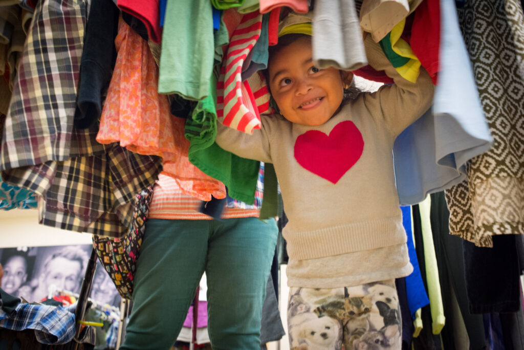 Young girl playing under a rack of colorful clothing