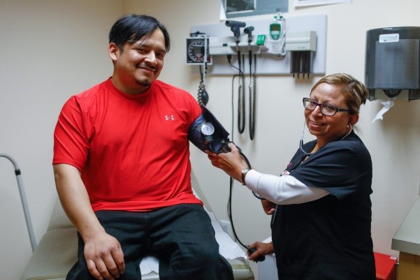 Female nurse taking the blood pressure of male patient wearing a red t-shirt